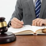 Prawnik w garniturze podpisuje dokument przy biurku z młotkiem sędziowskim